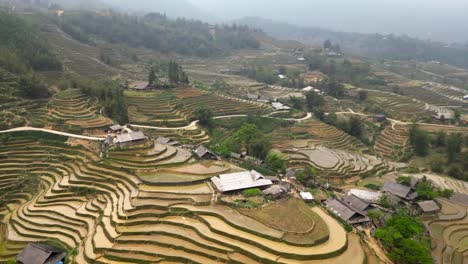 aerial view of mountainous terrain with layered rice paddies and stilted homes scattered across a quiet highland village during planting season in asia.