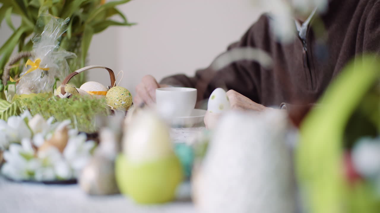 Mani di una persona che tengono un uovo di Pasqua decorato su una tavola festiva.
