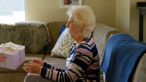 Granddaughter-giving-gift-to-her-grandmother-in-living-room-4k