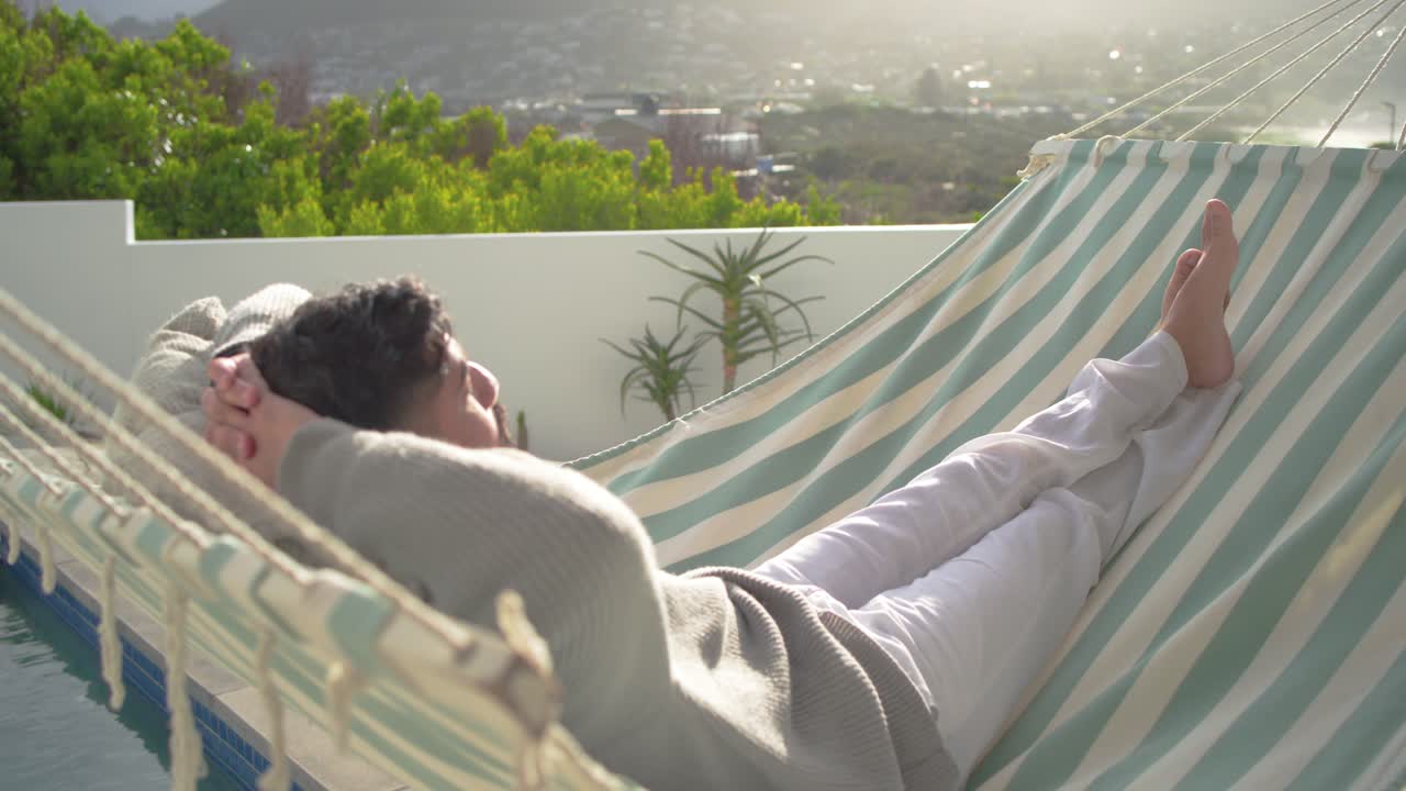 Striped hammock is swaying on rooftop pool terrace as camera is pushing closer, framing sunlit city