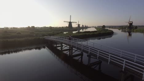 un dron disparó hacia la izquierda, alrededor de un modelo parado en un puente y mirando los molinos de viento holandeses en los países bajos durante el amanecer