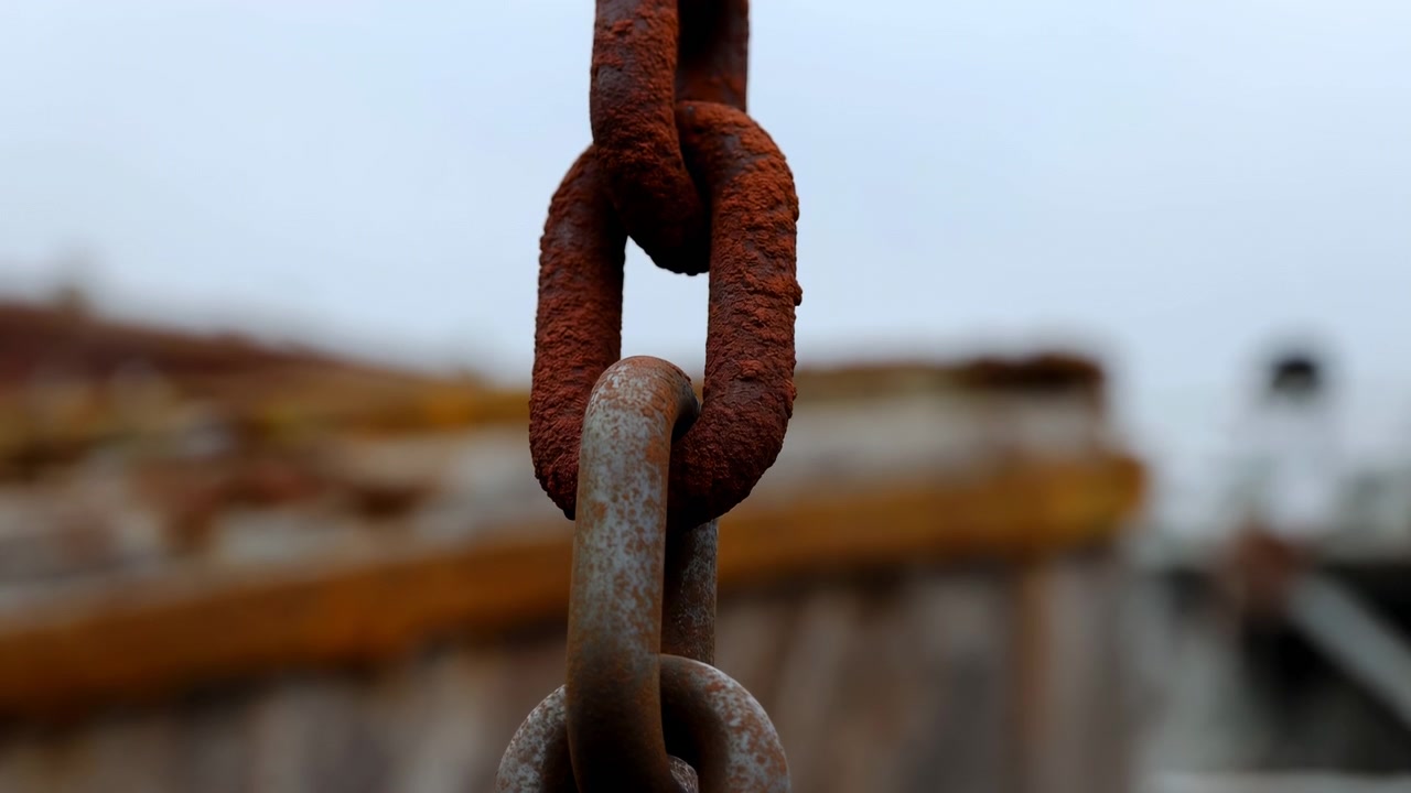 this close-up shot captures a rusty chain on an industrial construction site, showcasing a neutral atmosphere with metal structures and equipment. the scene features brown and gray tones.