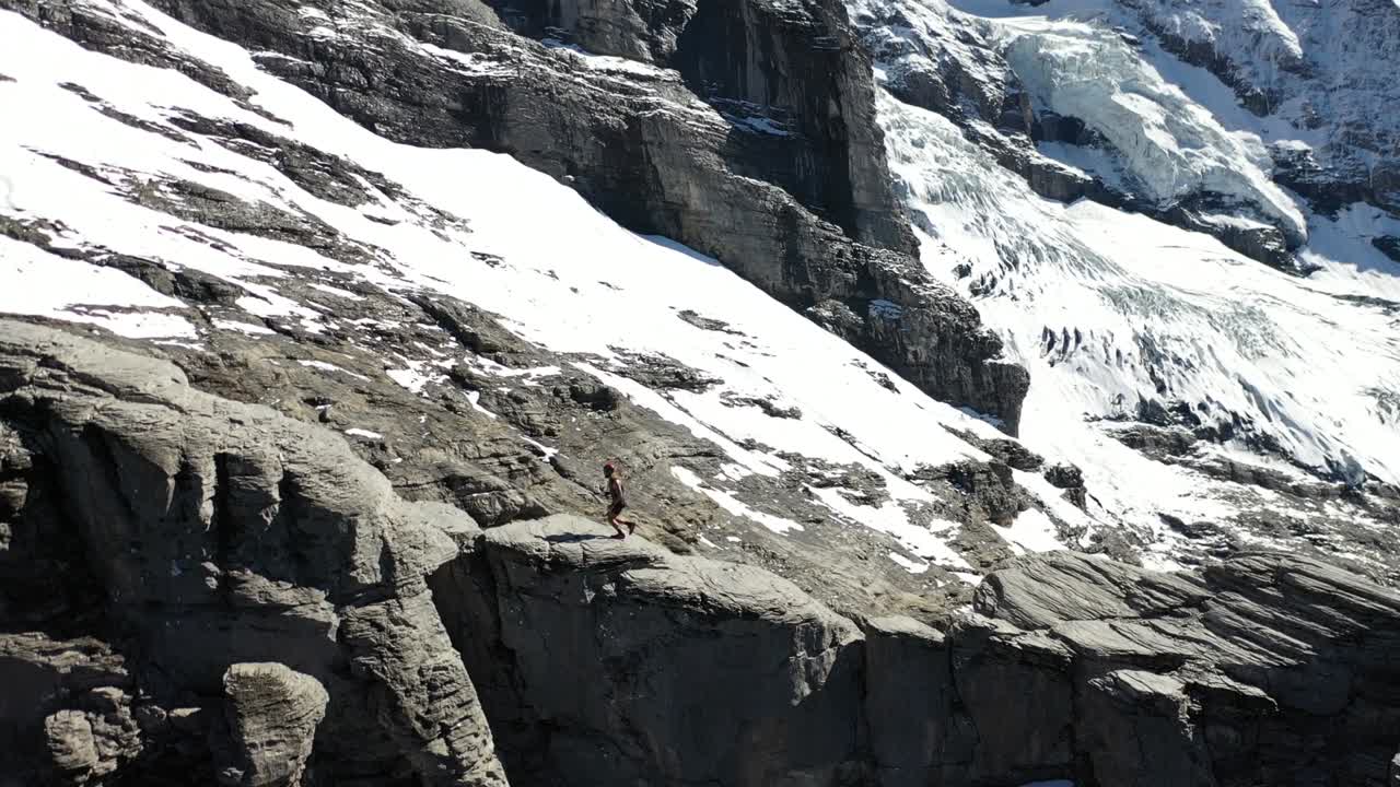 disparo de dron dando vueltas alrededor de un joven trotando, casi corriendo por las grandes rocas y acantilados en la parte superior de rotstock vía ferrata