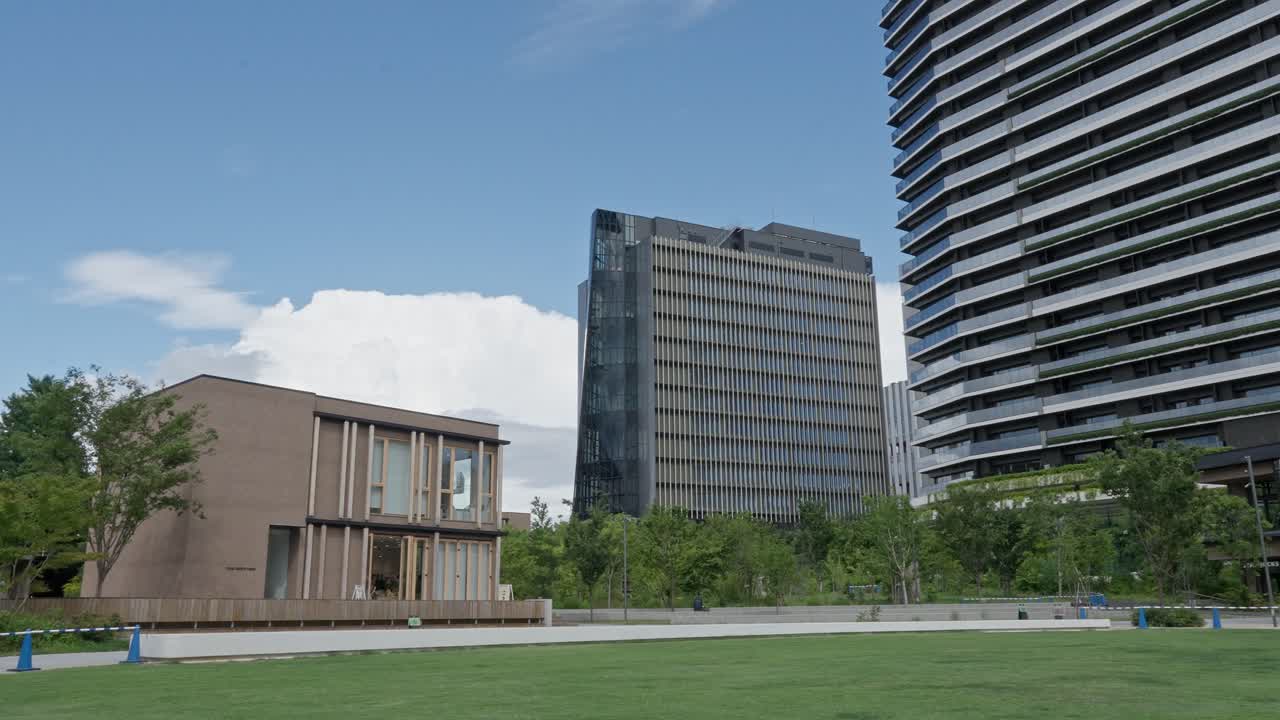 Modern architecture and green space blend in a city park with a low-rise building and skyscraper