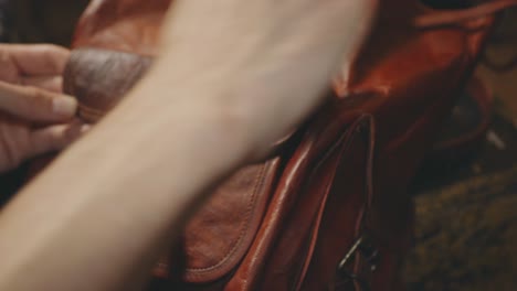 a woman's hands applying a polishing wax to her leather vintage backpack using a clean sponge - closeup shot