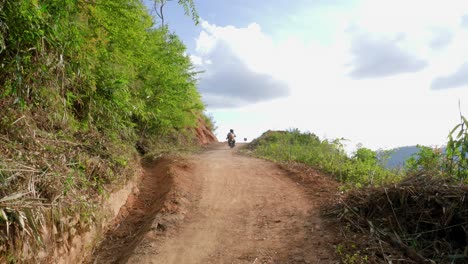 Male-and-female-couple-riding-moped-on-dirt-road-up-a-mountain-on-beautiful-day,-Vietnam