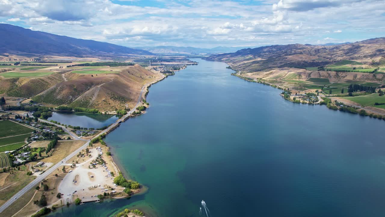Aerial shot of Lake Dunstan with hills, clouds, and small boat moving