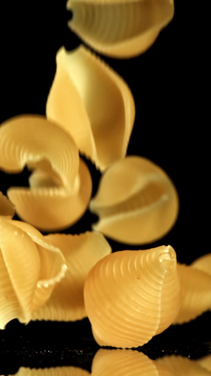 Raw Conchiglie Pasta Falling onto a Black Reflective Surface