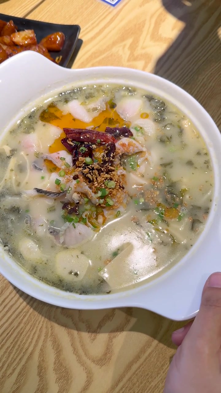 Vista dall'alto di zuppa di pesce piccante con olio al peperoncino servita su un tavolo di legno di un ristorante
