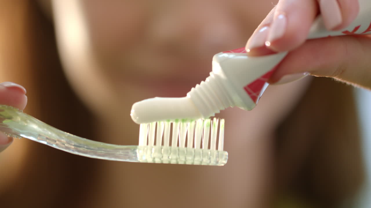 Escovação matinal dos dentes. Close-up das mãos de uma mulher apertando pasta de dente na escova.