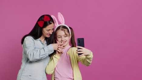 playful cheery mother and girl smiling for photos on smartphone