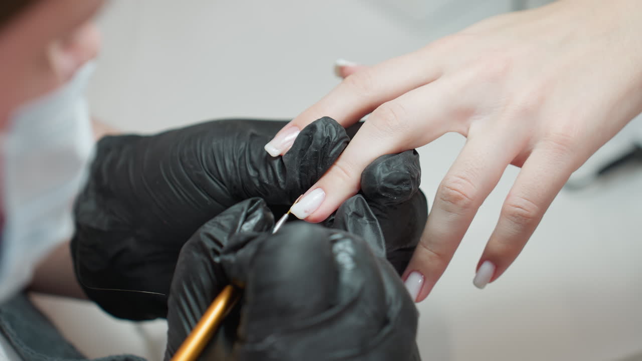 Nail technician wearing black gloves carefully applies white acrylic on client fingernail using precision brush, highlighting attention to detail and clean, professional salon environment