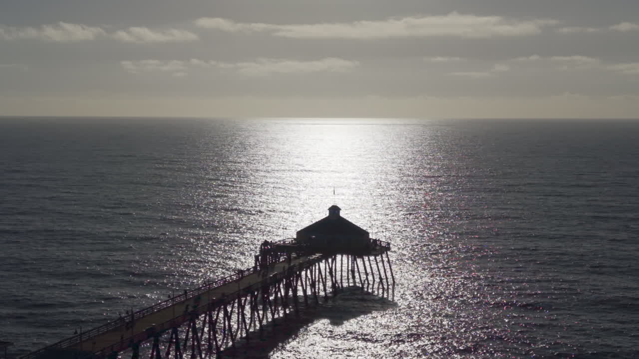 Silhouette of the Imperial Beach Pier. Bright sunlight reflection on the ocean, drone view
