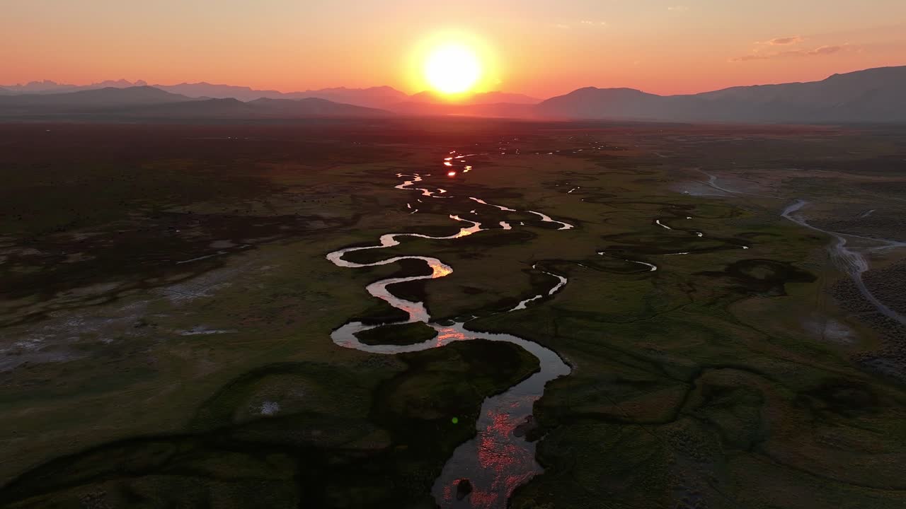 Drone pushes in toward the setting sun over the meandering Owens River near Mammoth Lakes California. Golden hour light glows on S curve channels and open valley with distant Sierra peaks