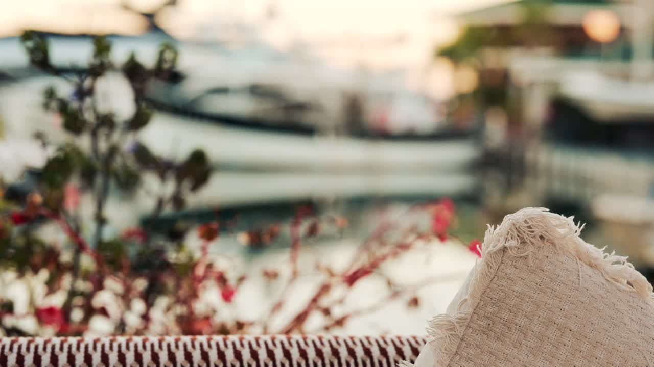 Cozy outdoor sofa with textured cushion in the foreground, overlooking a blurred marina with yachts and boats in soft evening light