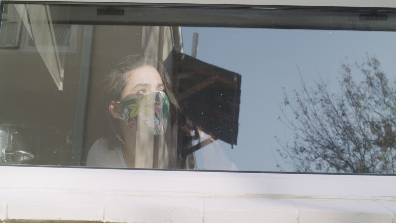 mujer mirando por una ventana, con una máscara