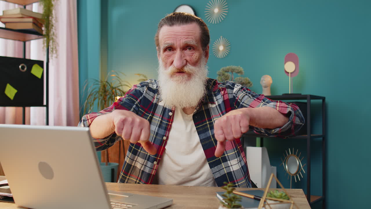 hombre de edad avanzada trabajando en una computadora portátil en la oficina de casa mostrando los pulgares hacia abajo señal de desaprobación