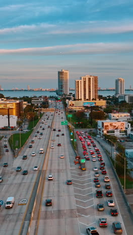 lots of cars move by the multi-lane highway and stand in the congestion. drone footage above miami, florida at sunset. vertical video