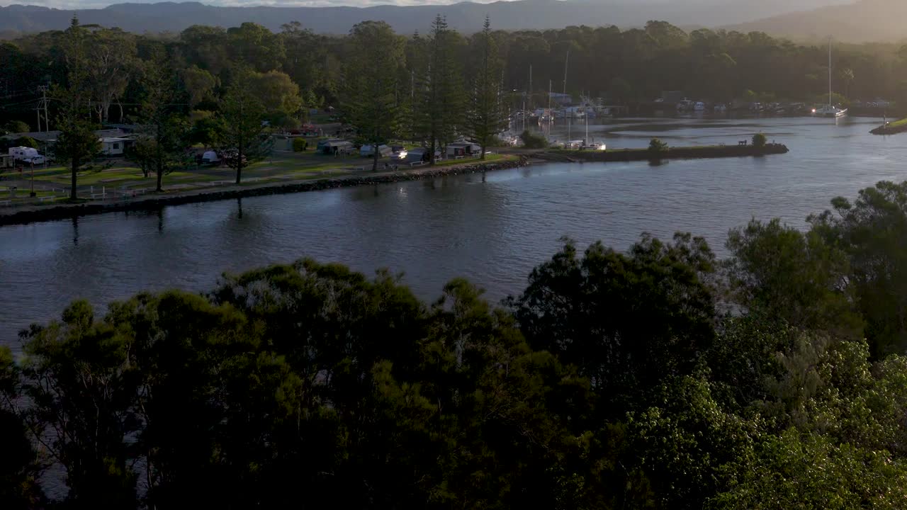 Aerial footage captures the tranquil Brunswick Heads river at sunset, highlighting lush greenery and calm waters under soft lighting
