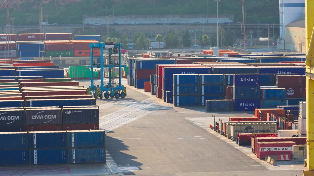 Grande gru a portale che si muove attraverso un trafficato porto industriale con pile di container, mostrando la logistica globale, il commercio e il trasporto merci in un porto commerciale.