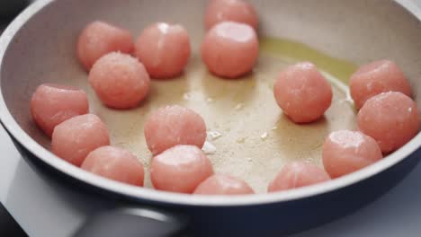 crop person adding meatballs to frying pan