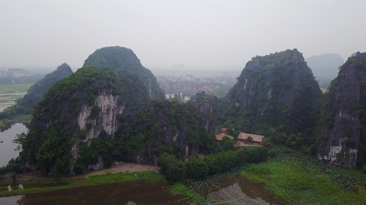 Discover the captivating scenery of Ninh Binh, Vietnam, where expansive rice plantations lie nestled at the base of impressive, verdant rock formations.