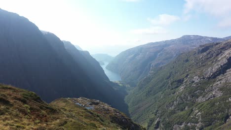 beautiful woman standing on top of cliff surrounded by dramatic landscapes and complete wilderness in norway mountains - aerial close to person at kiellandbu norway