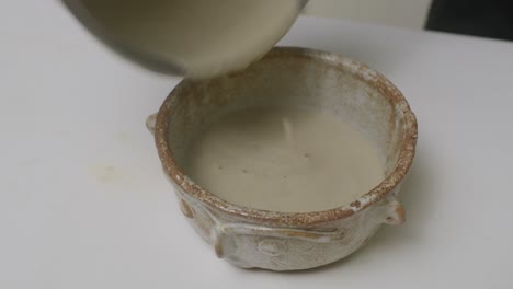 pouring mashed onion soup into stylish ceramic bowl