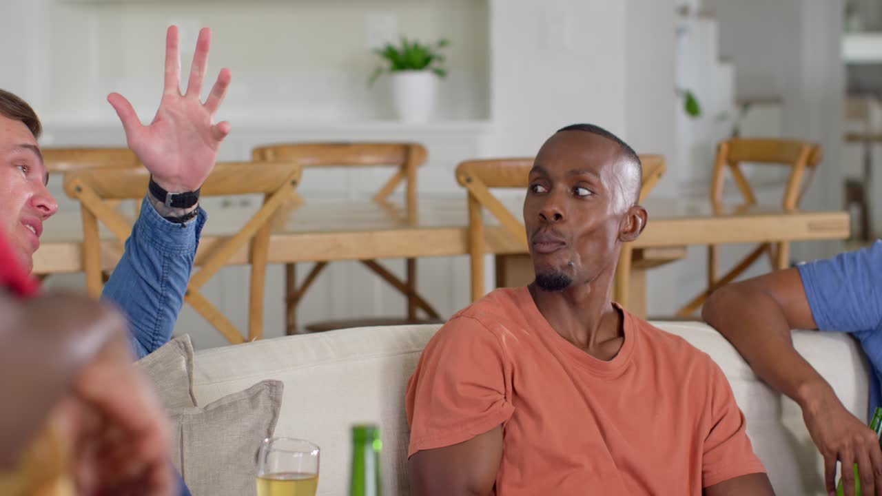 Vertical video: Reacting man in orange tee snacking while bald man talking at home, with beers