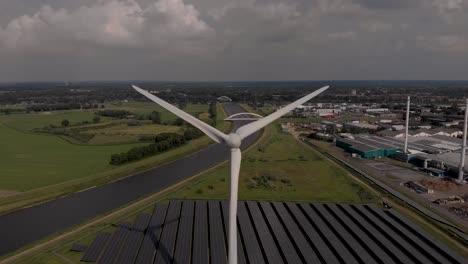 aerial panning sideways showing a wind turbine with solar panels, biofuel and water recycling facility in dutch waterway infrastructure landscape