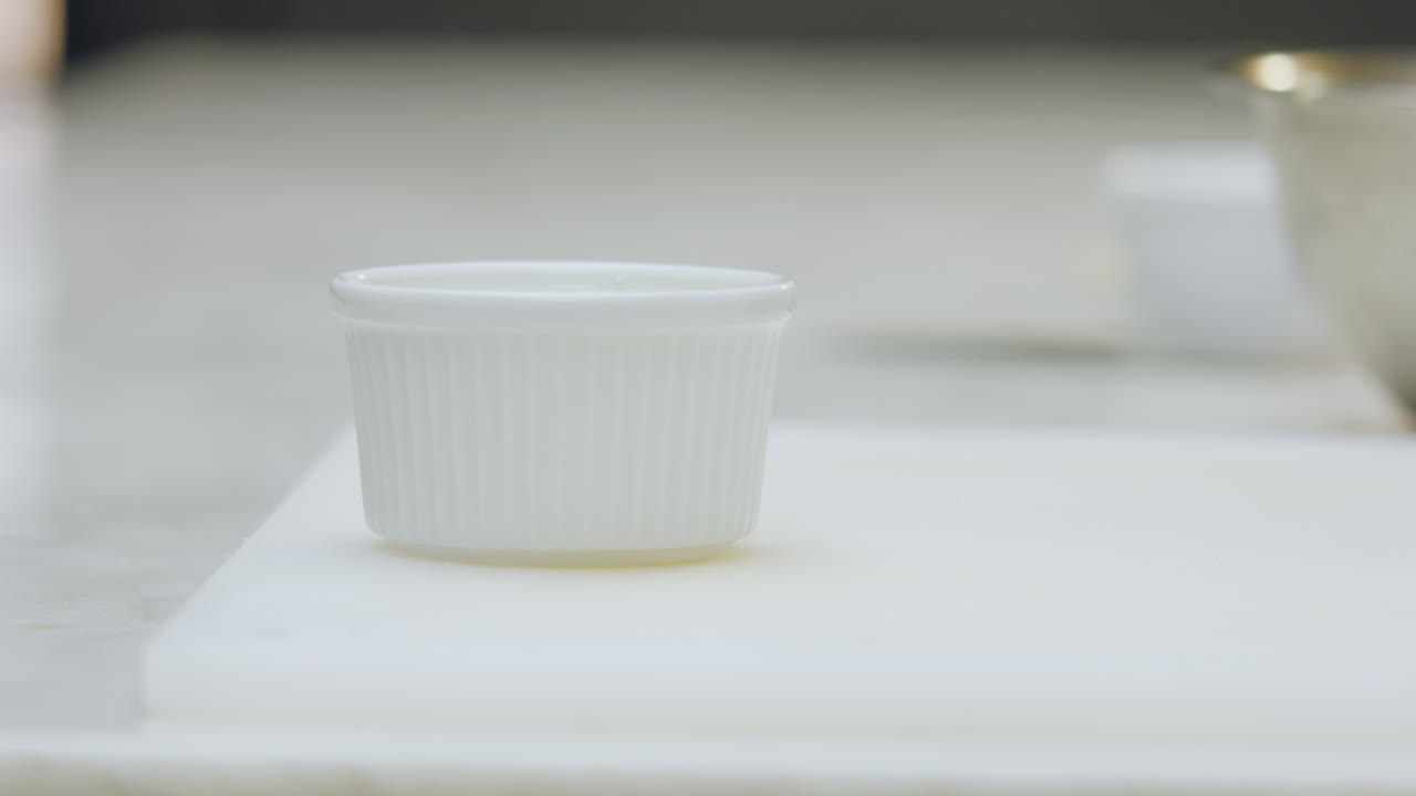 Close-up of a chef transferring crema catalana from an aluminum mold to a ceramic one using a spatula, in the preparation of a creme brulee dessert