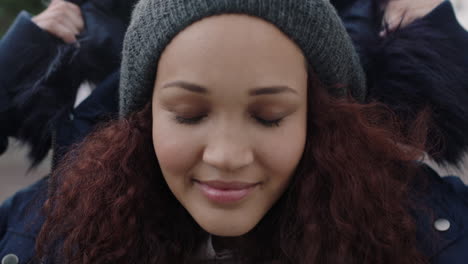 close up portrait of young beautiful mixed race woman with frizzy hair smiling enjoying wearing beanie fur coat looking at camera