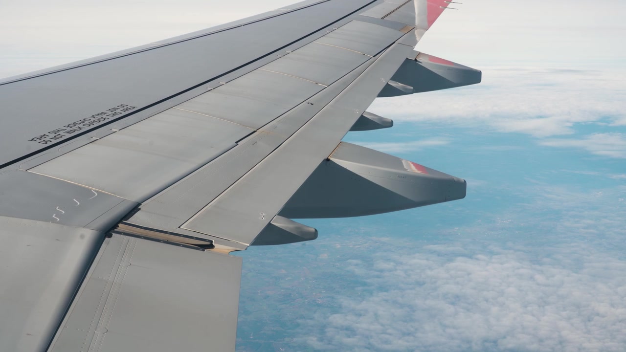 Ala di un aereo passeggeri che vola sopra nuvole bianche e spesse sotto un cielo blu, vista aerea