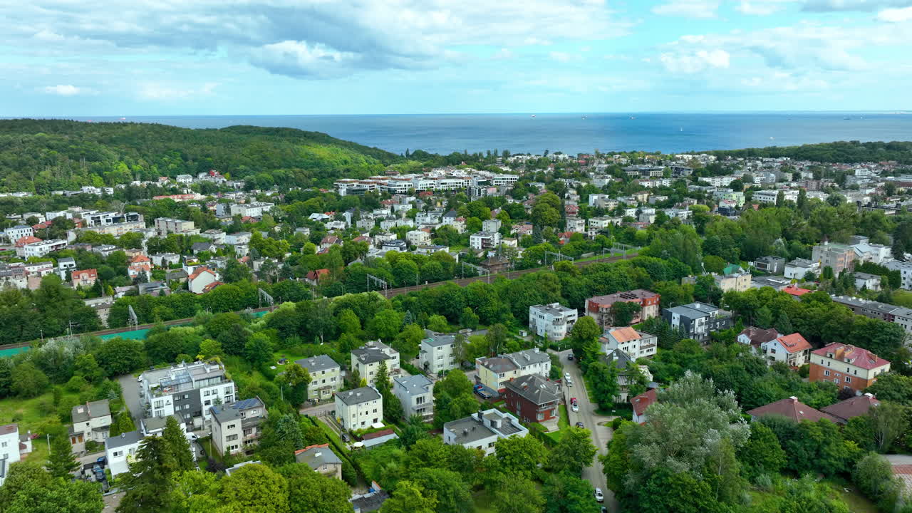 gdynia orłowo의 넓은 공중 촬영, 밀집된 초록색, 주거 지역, 그리고 바르티크 해가 지평선으로 어있는 것을 강조합니다.