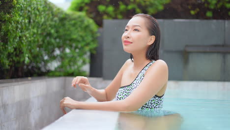 close-up of a young woman leaning on the edge of an infinity-edge swimming pool checking out her surroundings