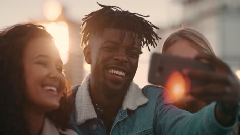 happy multi ethnic friends enjoying rooftop party drinking alcohol taking selfie photos using smartphone sharing fun weekend on social media at sunset