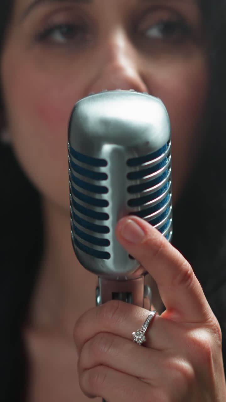 Close-up of a serious female vocalist in a black outfit, gripping a vintage microphone with one hand, as the camera zooms in against a blurry background