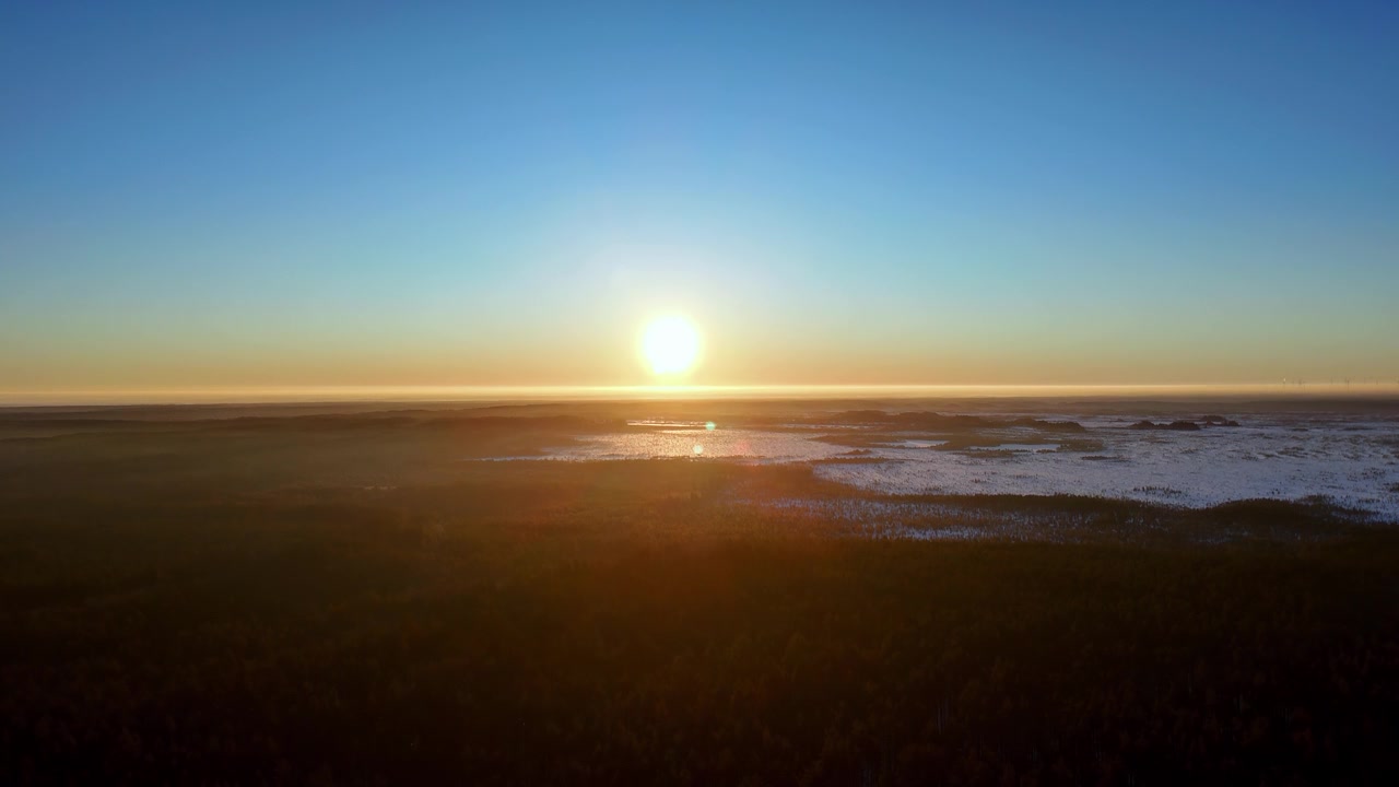Vast frozen wetlands transition into golden morning light during a serene winter sunrise over the arctic wilderness captured from a high altitude drone perspective featuring clear skies and warm hues