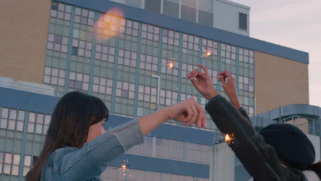 slow motion beautiful young women friends holding sparklers celebrating new years eve on rooftop at sunset dancing having fun enjoying holiday party celebration