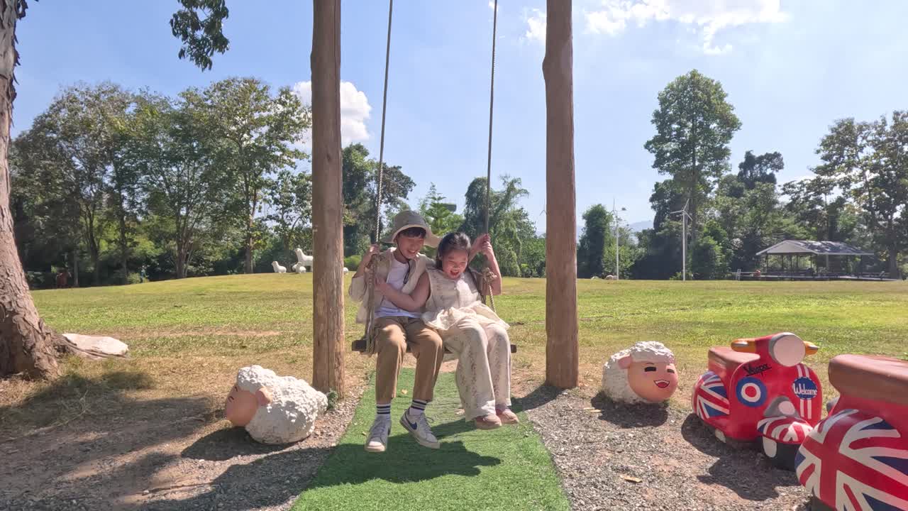 Due giovani bambini asiatici giocano su un'altalena di legno in un parco verde e soleggiato