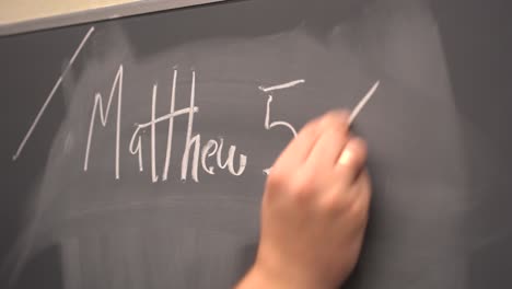 caucasian hand writing on chalkboard matthew 5-6