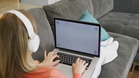 A-caucasian-teenager-girl-with-headphones-using-laptop-with-copy-space-at-home,-slow-motion