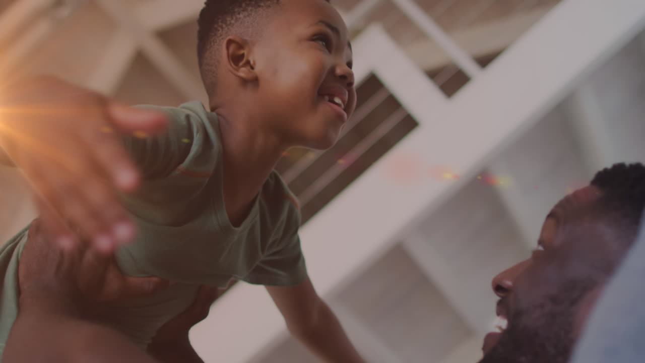 Animation of lights over happy african american father and son having fun at home