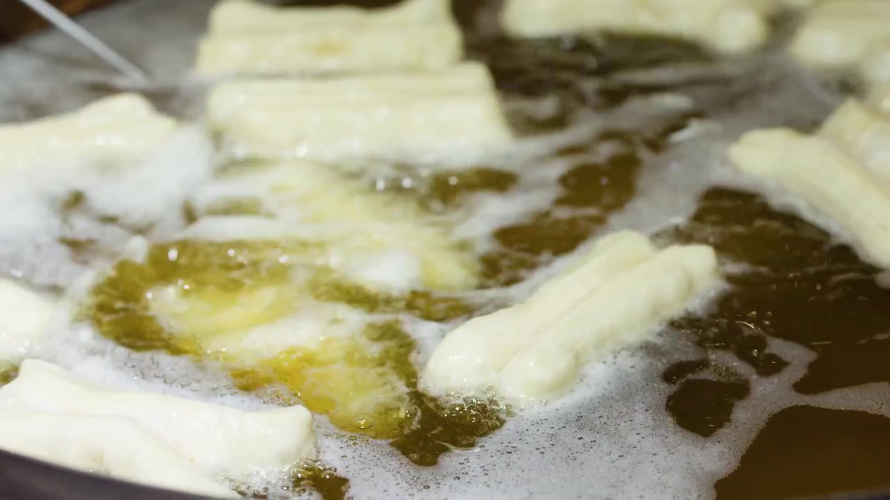 Close-up of youtiao dough frying in bubbling oil within a large wok at breakfast.