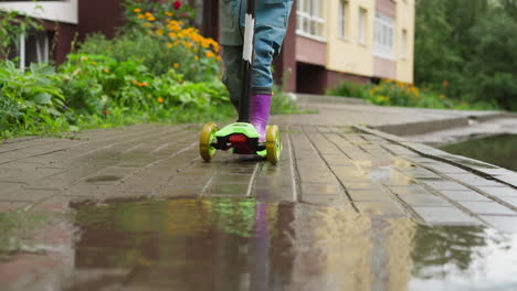 kid dashes through raindrops on scooter child in rubber boots stops in front of puddle on pavement