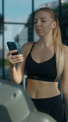 woman using smartphone on treadmill in gym