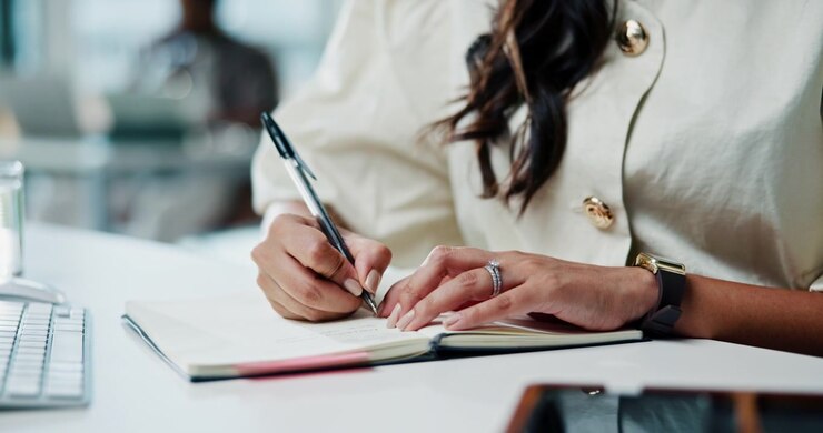 Woman Writing in a Notebook at an Office Desk