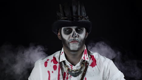 sinister man with halloween skeleton makeup in shirt with blood looking at camera, trying to scare