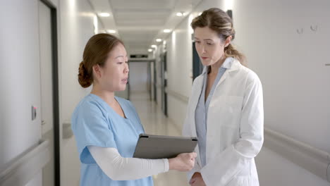 retrato de mujeres diversas y felices discutiendo con una tableta en el pasillo del hospital, en cámara lenta