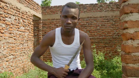 un joven gángster africano sostiene un cuchillo en un edificio abandonado en áfrica rural